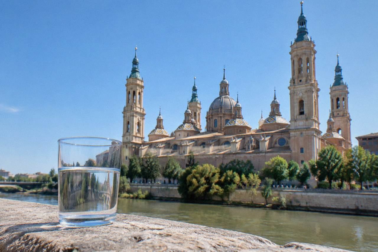 A glass of water standing on a stone ledge with the Basilica del Pilar rising behind it in daylight