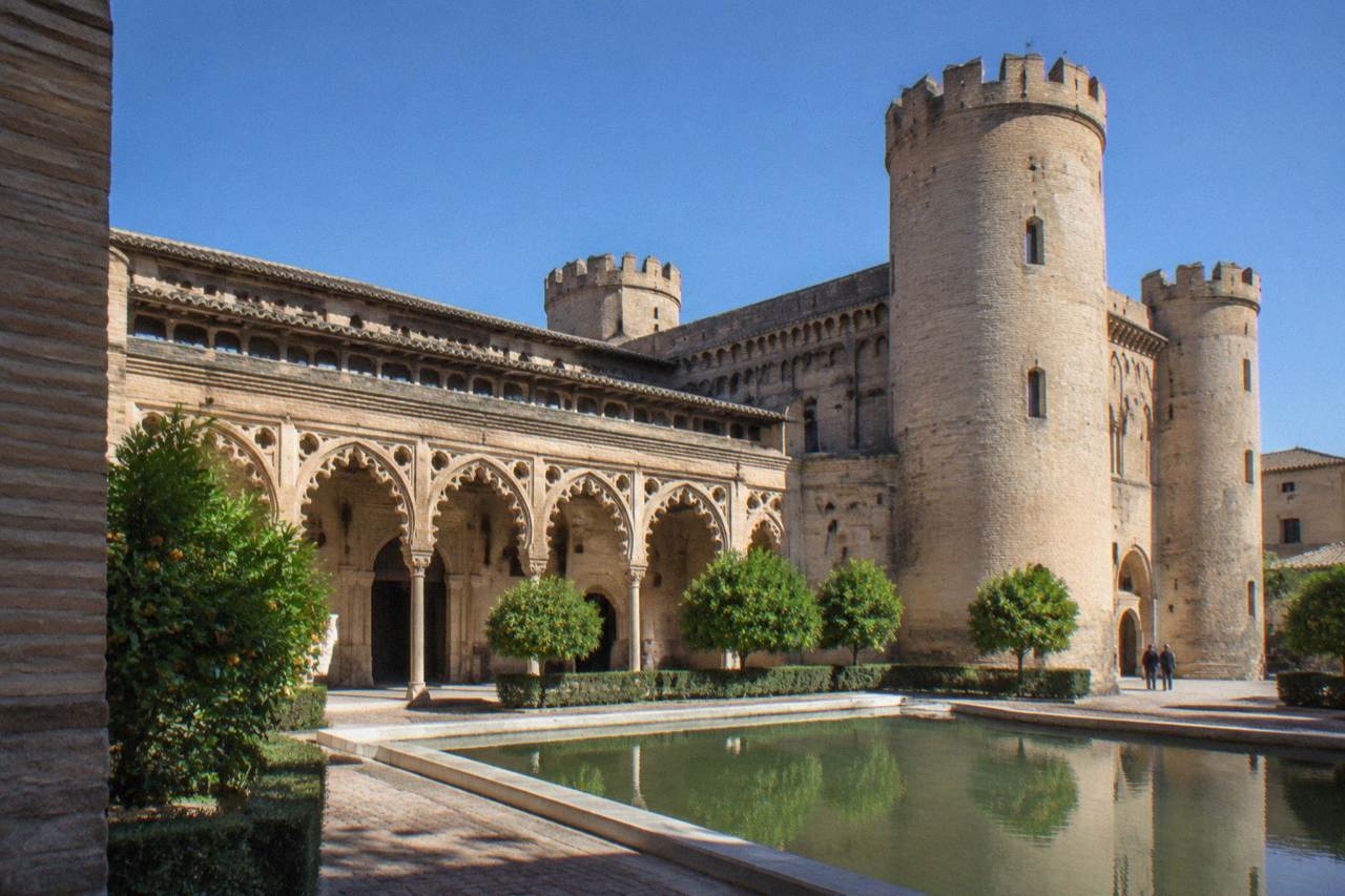 The ornate brick facade and cylindrical towers of the Aljafería Palace in Zaragoza under a clear sky