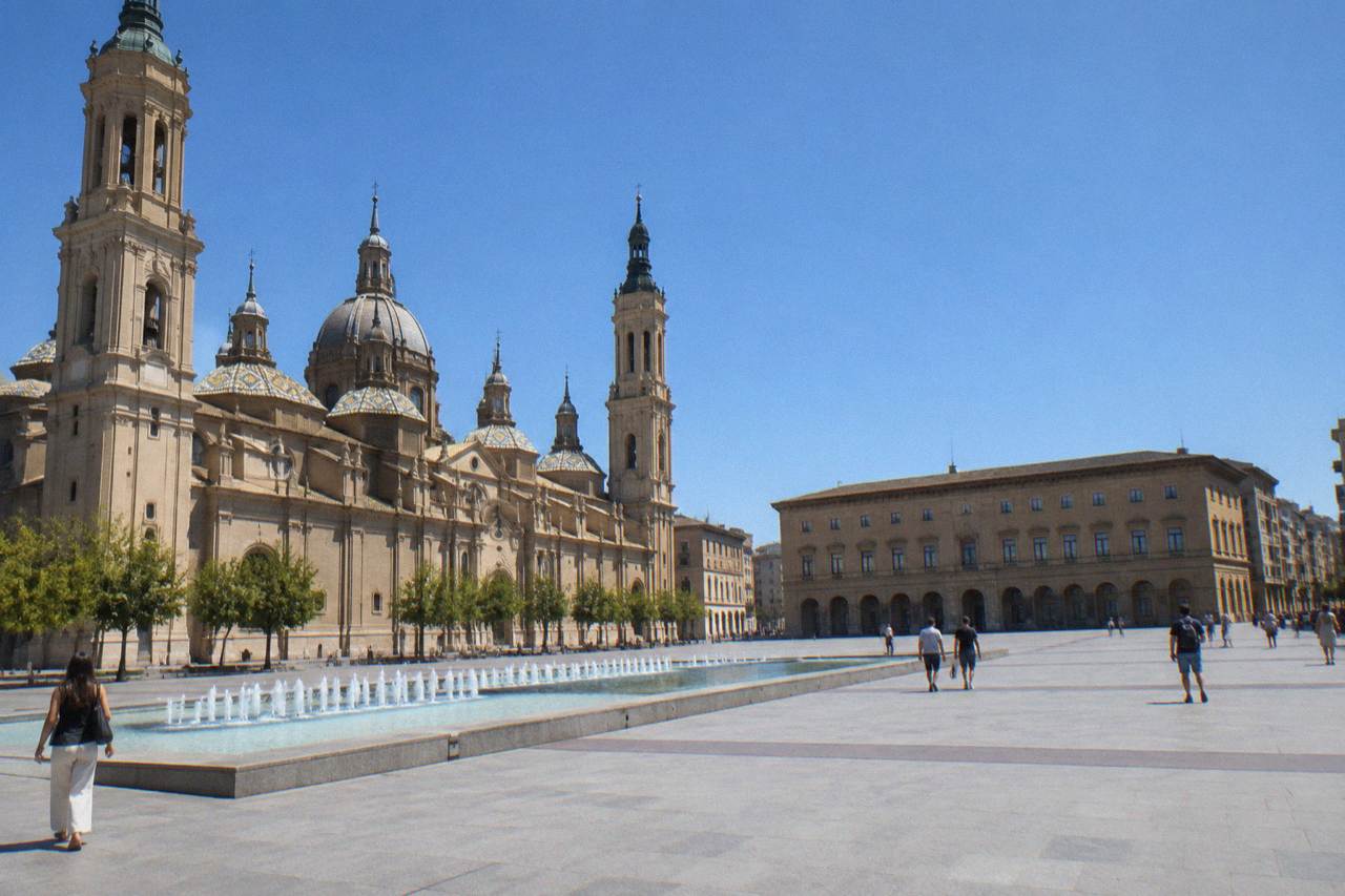 Visitors reading a menu board on a sunlit street in the old town of Zaragoza