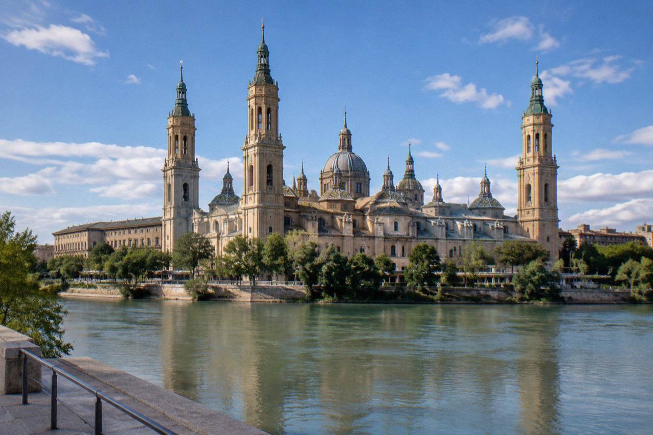 The Basílica del Pilar and its domes seen across the Ebro river under a partly cloudy sky in Zaragoza