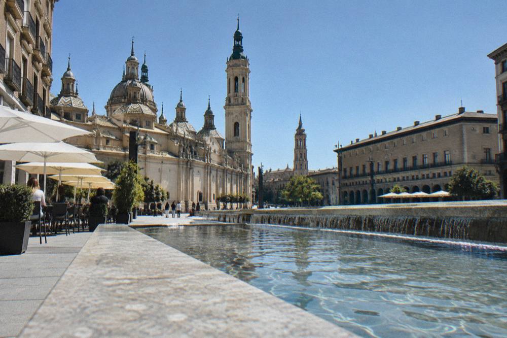 A stone street in the Zaragoza old town with bar terraces and the tower of La Seo visible above the rooftops