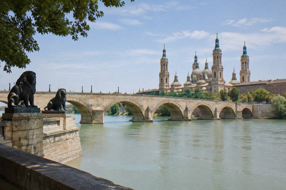 The wide Ebro river flowing under the stone arches of Zaragoza's Puente de Piedra at midday