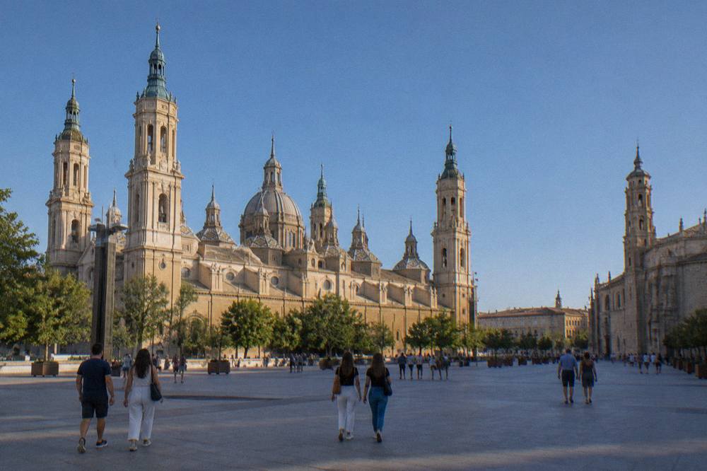 Visitors walking across Plaza del Pilar between the Basílica del Pilar and La Seo on a sunny afternoon