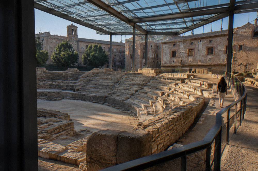 A visitor walking beside the stone seating rows of the Roman theatre excavation in Zaragoza
