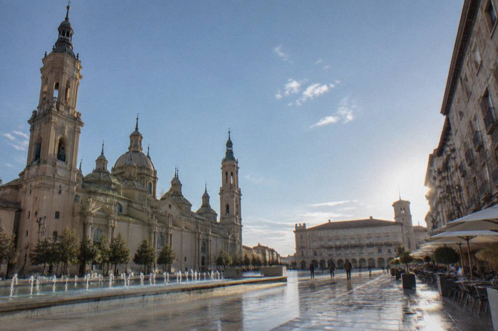 A street of cafe tables and stone buildings in Zaragoza's old town on a bright afternoon