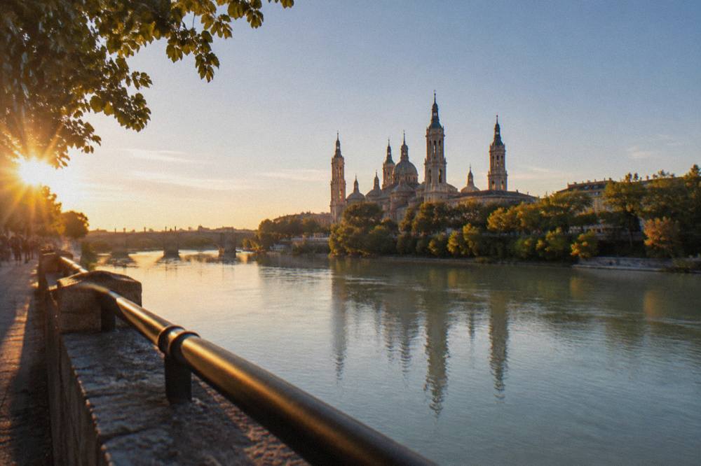 View across the Ebro river towards the domes and towers of the Basílica del Pilar at golden hour