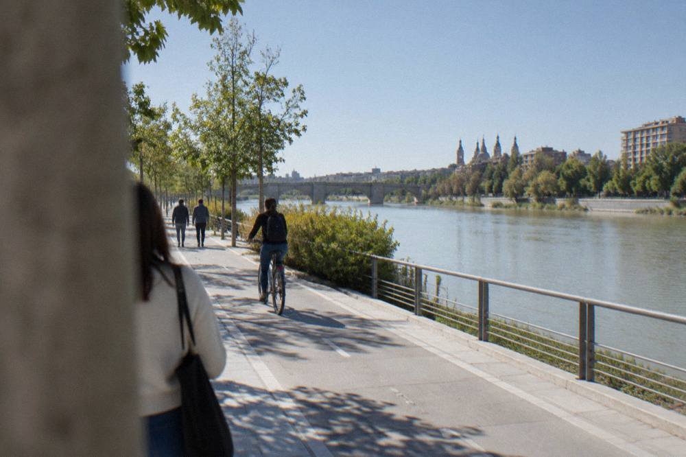 People walking and cycling on a riverside path beside the Ebro in a modern district
