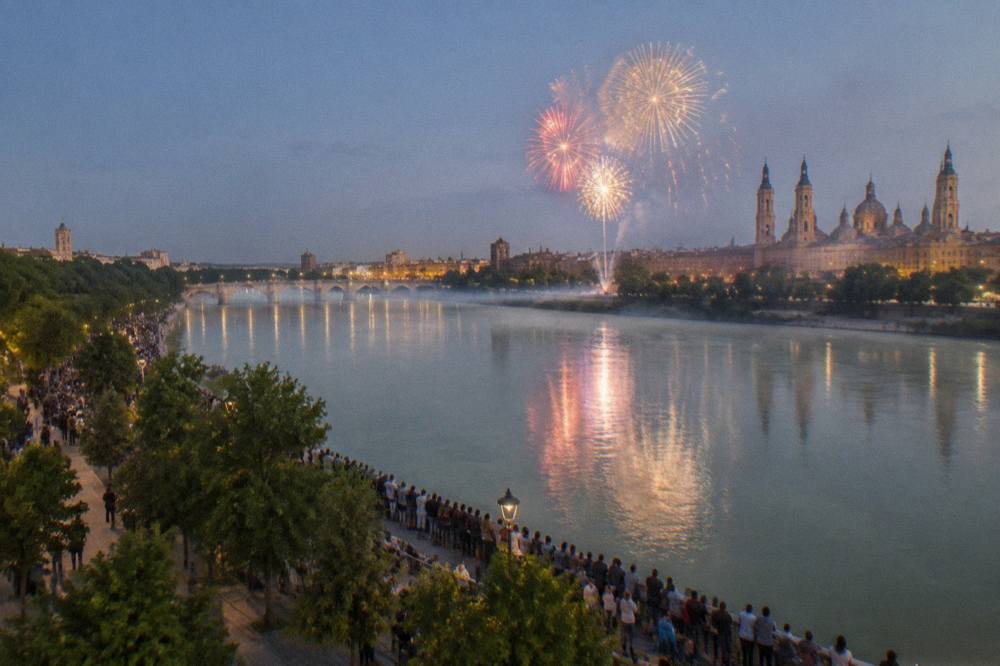Crowds watching fireworks over the Ebro river with city lights in the background