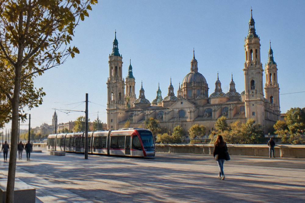 A Zaragoza tram passing along a central street with the basilica towers in the distance