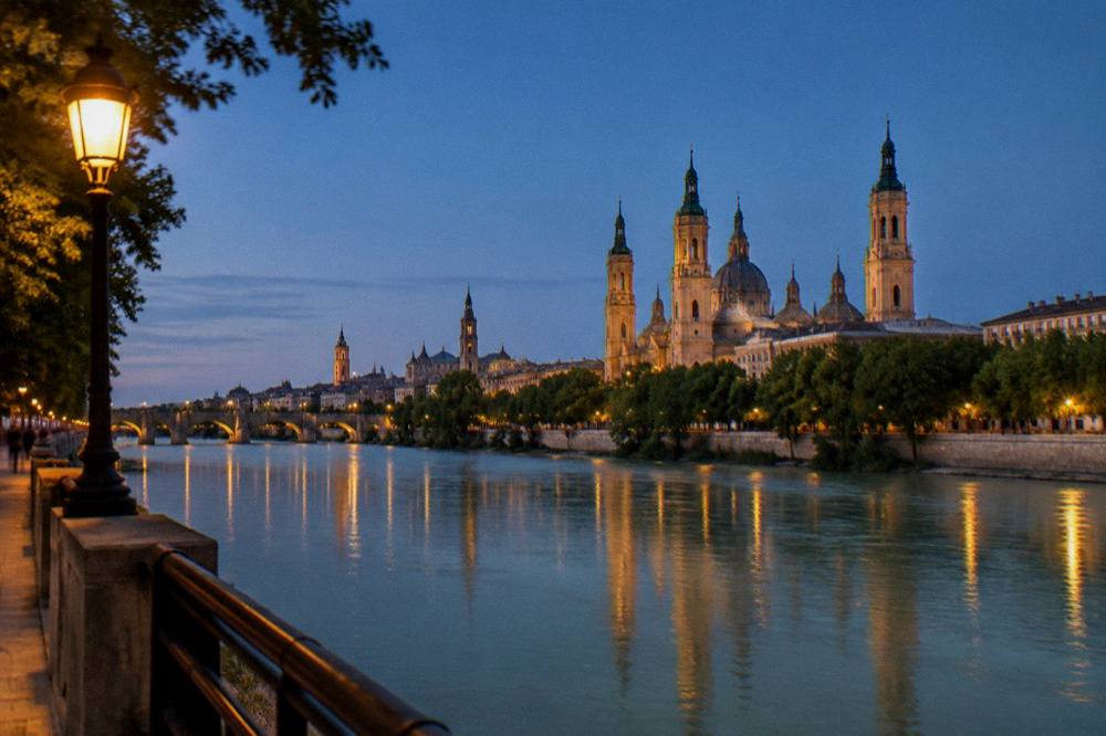 The Zaragoza skyline at dusk with the towers of the old town and the Ebro river in the foreground