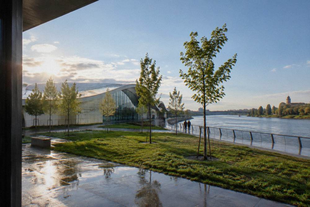 Modern glass pavilion building beside a wide river bend under a clear sky