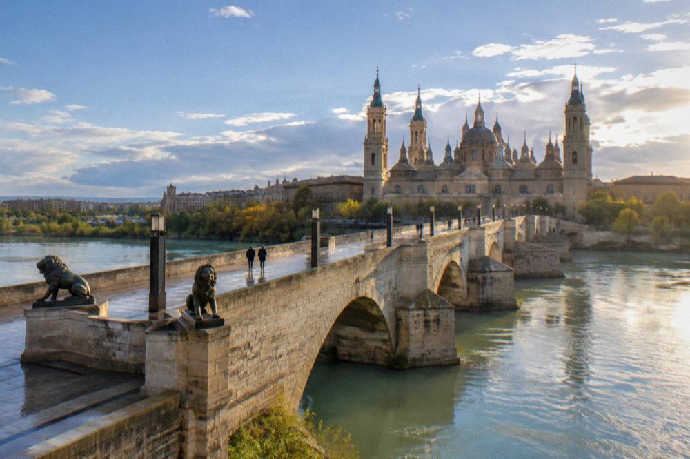 Ornate baroque basilica dome and towers seen across a wide stone bridge