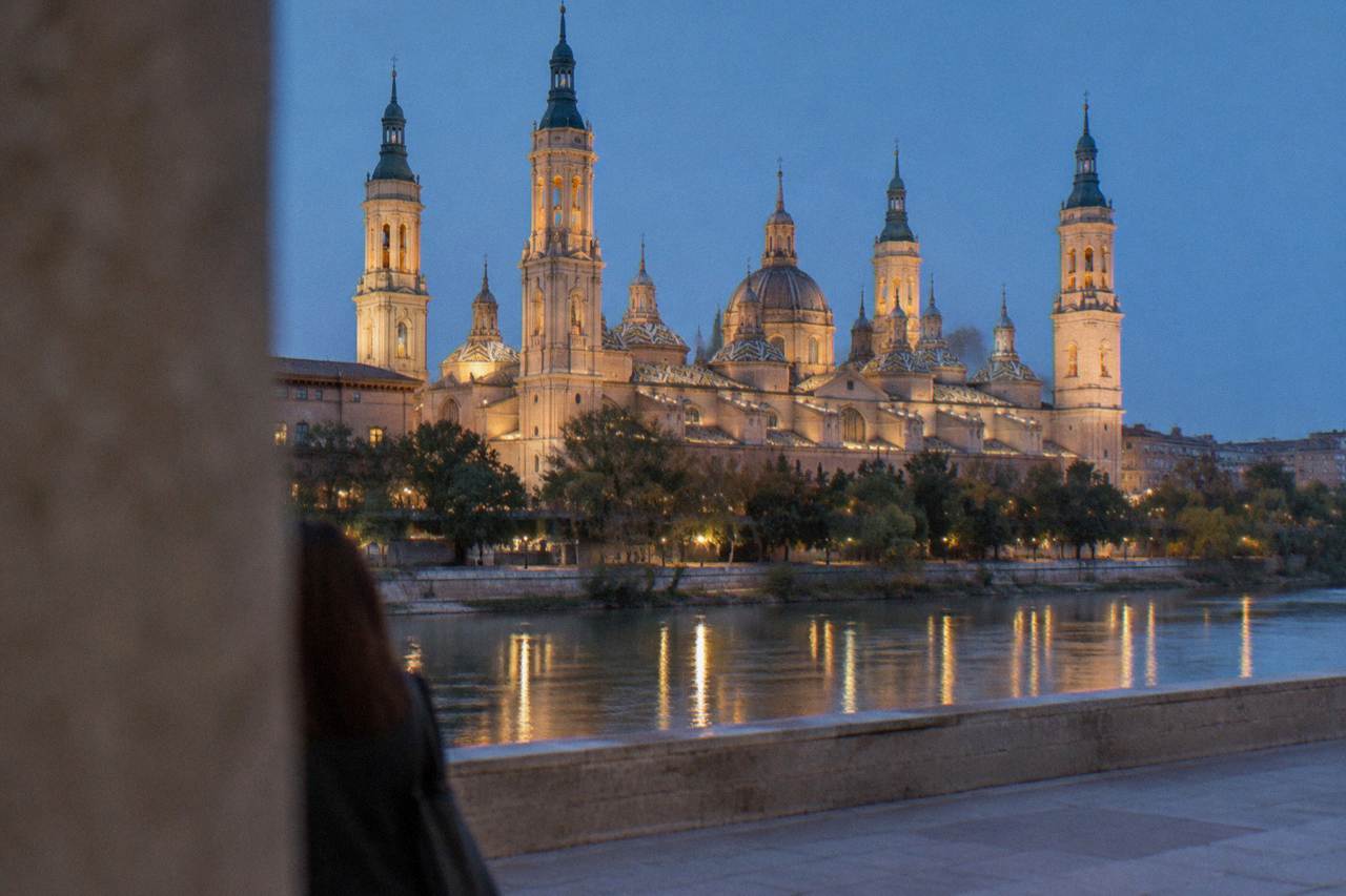 The Basílica del Pilar seen from across the Ebro river at dusk, with its domes and towers lit against the sky