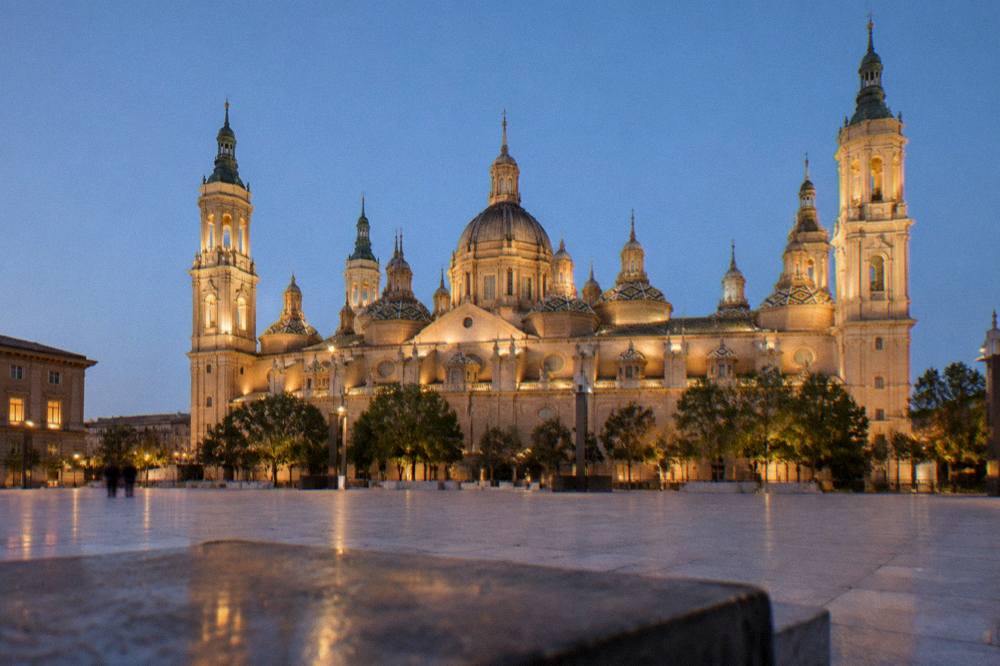 The basilica illuminated at night with its domes glowing above the empty square