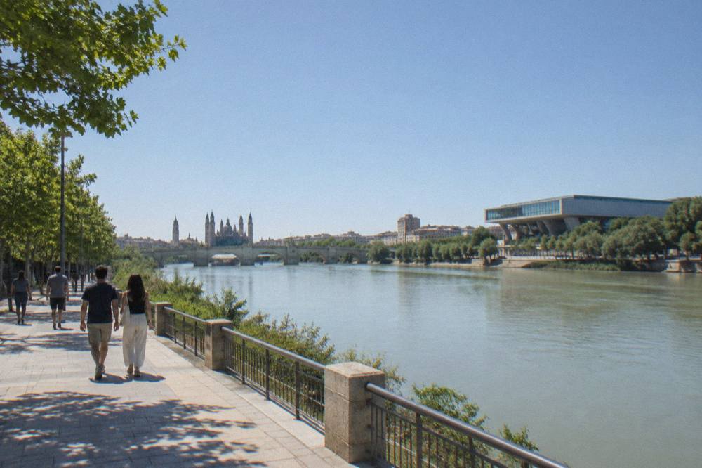 People walking along the Ebro riverbank path with a modern bridge building in the background