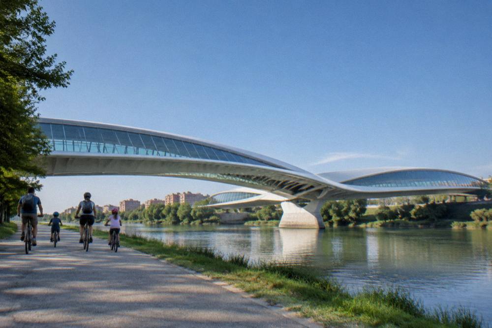 A family cycling together on a riverside path beside a modern bridge