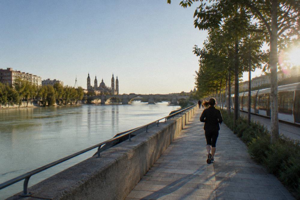 A tram passing near the riverbank with the Ebro and city buildings behind