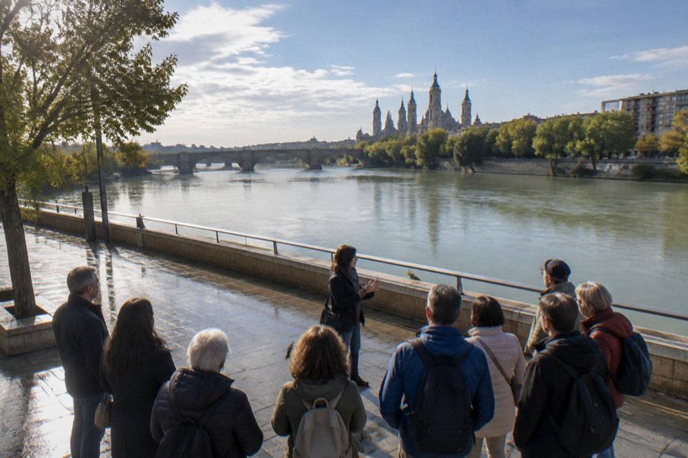 A guided tour group listening to a guide on a Zaragoza riverside square near the Ebro