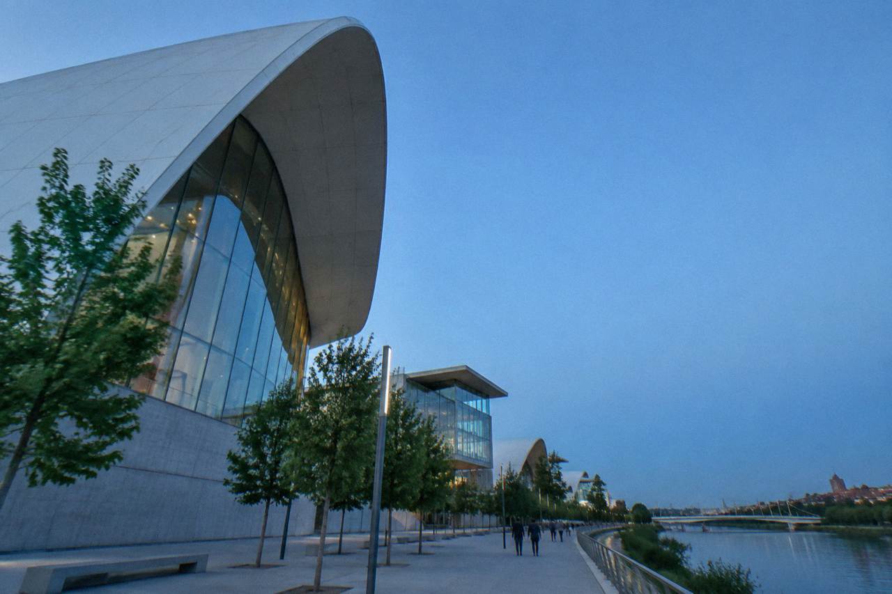 Modern concrete and glass pavilions of the Expo 2008 site beside the Ebro river under a clear blue sky
