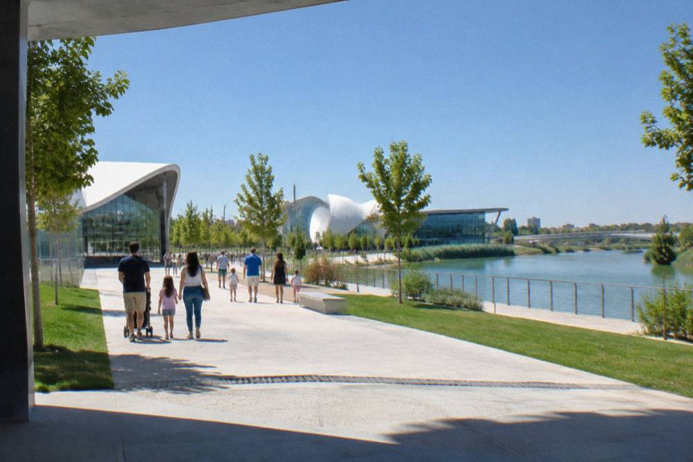 Families walking along a wide paved promenade between lawns and modern pavilions in the Expo park