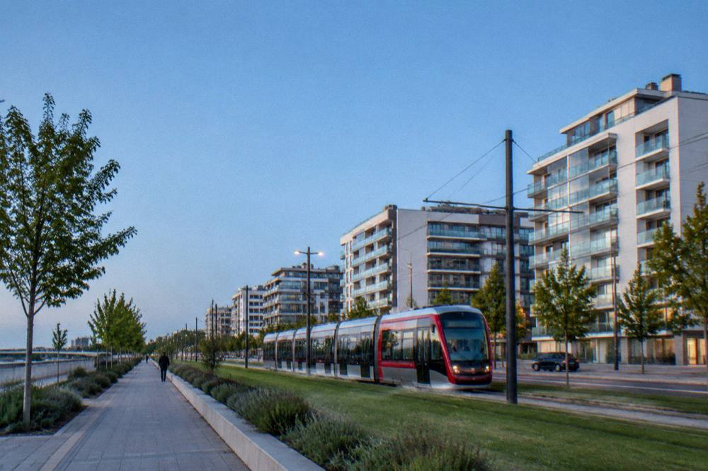 A modern tram passing glass apartment buildings on a wide avenue in the Actur district