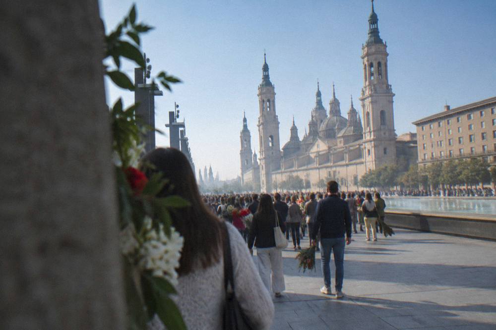 A crowd holding flowers on a busy street during a festival in Zaragoza
