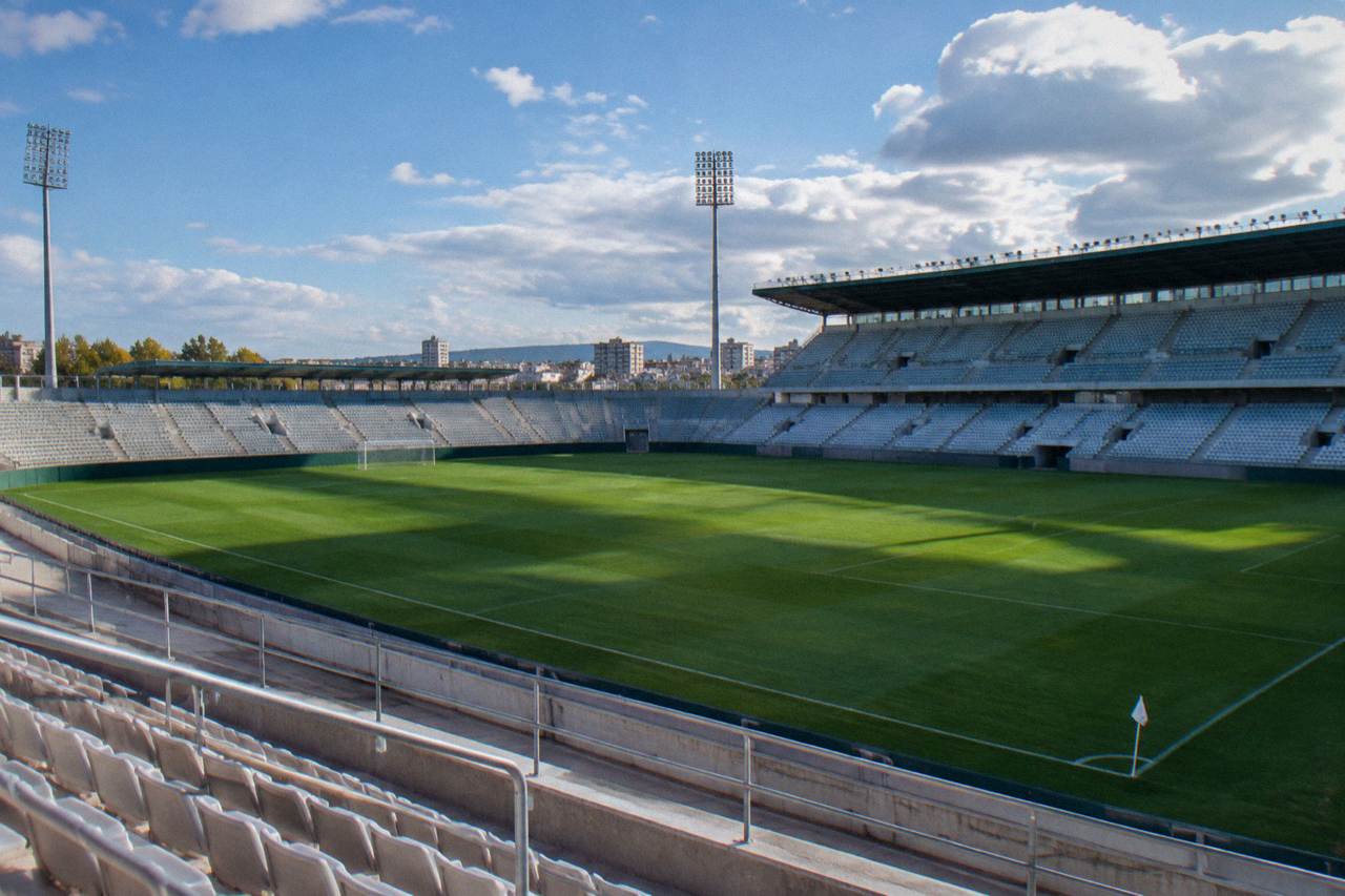 A large football stadium with tiered stands rising above a green pitch under a wide sky