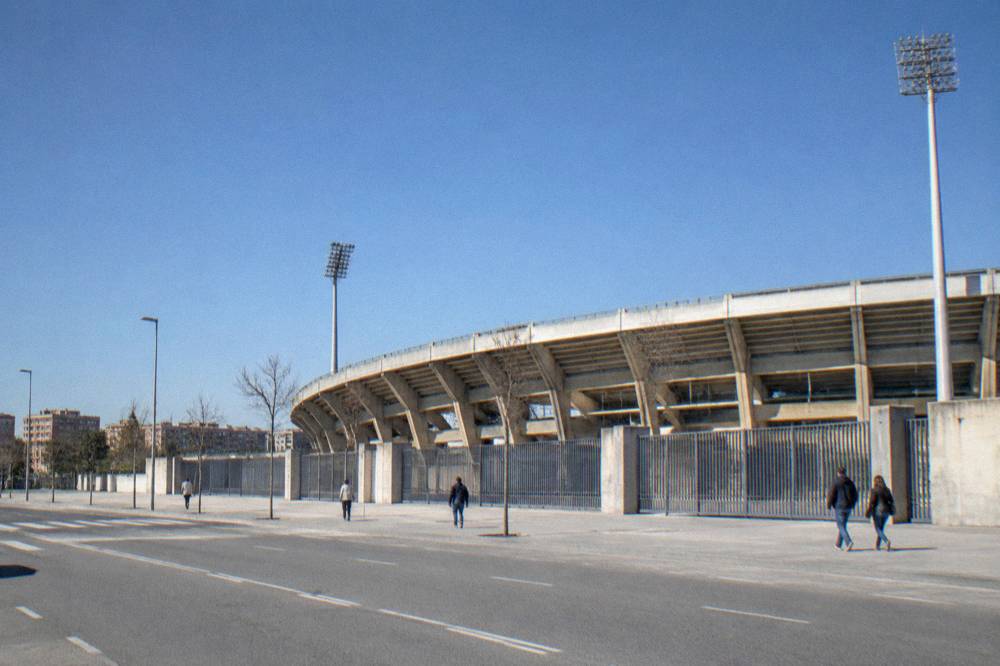 A quiet street outside a football stadium with closed gates and a few people walking past