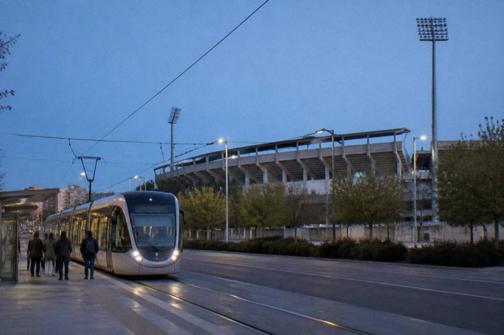A modern tram travelling along a street in a Spanish city with passengers waiting at a stop