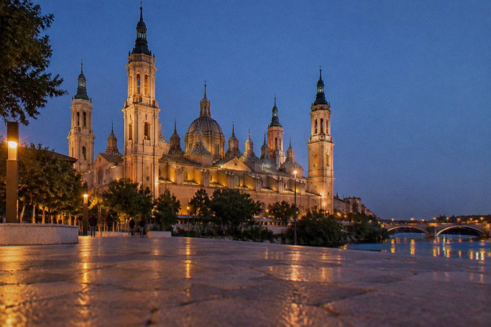 A wide view of a Spanish city skyline with a large basilica tower rising above rooftops in evening light