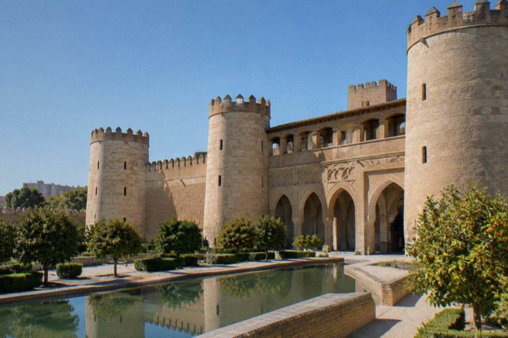 The fortified walls and towers of the Aljafería Palace under a clear sky in Zaragoza