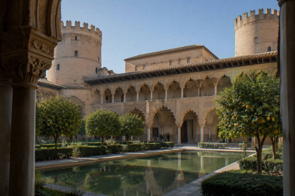A grand Moorish palace courtyard with ornate carved arches lit by afternoon light