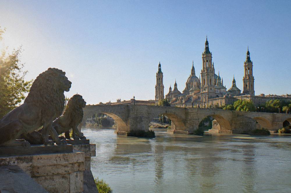The stone arches of the Puente de Piedra bridge over the Ebro river with the Basilica del Pilar behind