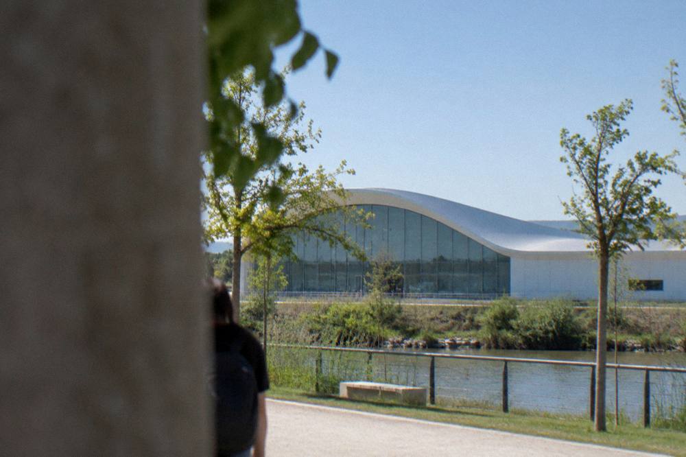 A modern aquarium building with a glass facade beside riverside parkland
