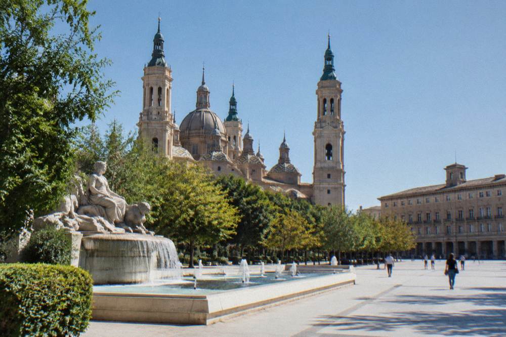 Stone fountain with sculpted figures surrounded by trees in a Zaragoza park