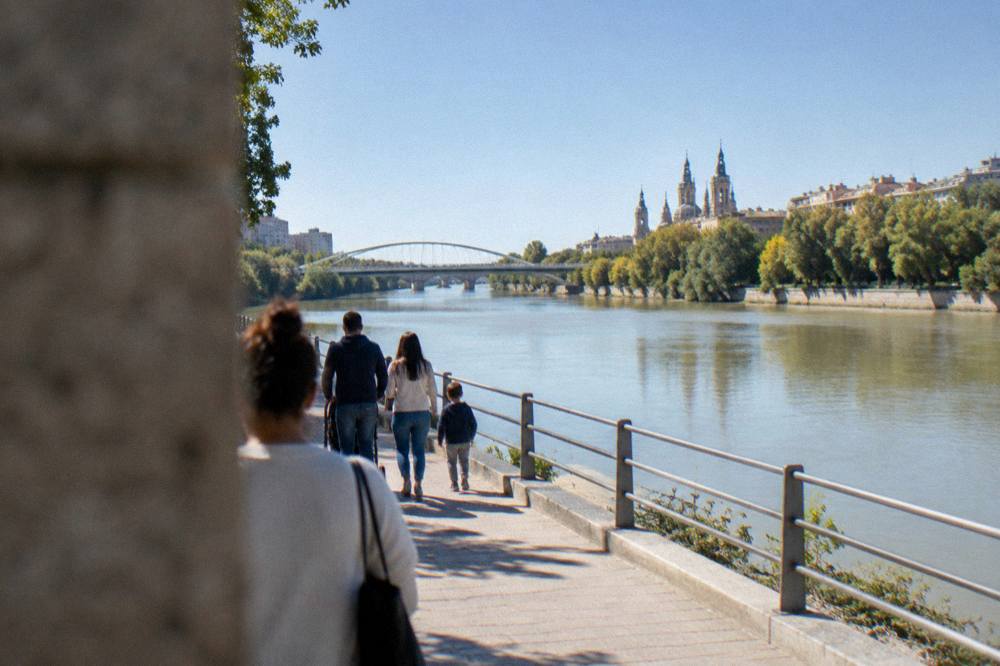 Families walking on a riverside path beside the Ebro in Zaragoza with modern bridges in the distance