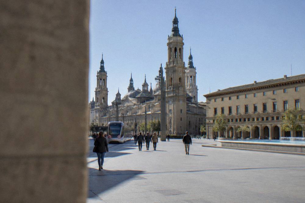 A tram and pedestrians on a street leading toward the basilica in central Zaragoza