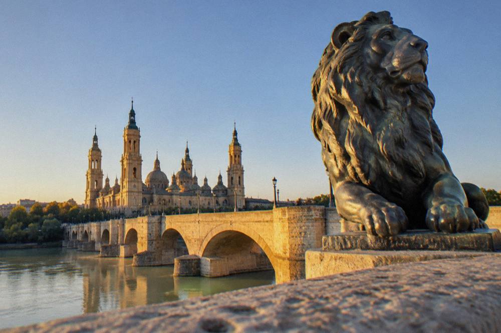 One of the bronze lions at the end of the Puente de Piedra seen close up against the sky