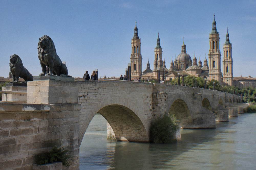 People walking across the stone bridge in late afternoon light with the basilica behind