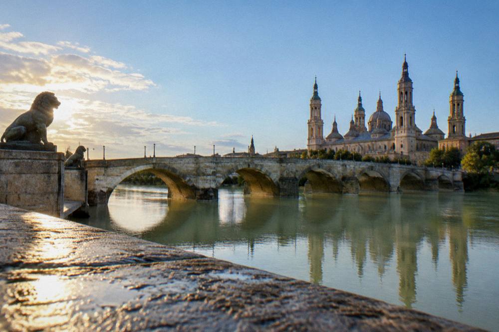 The stone bridge arches reflected in the calm water of the Ebro at dawn