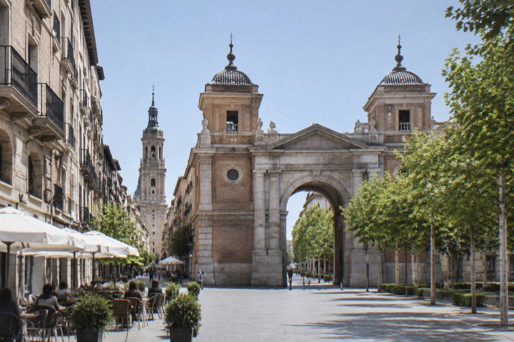 A narrow old-town street with café tables and stone buildings leading towards a church tower