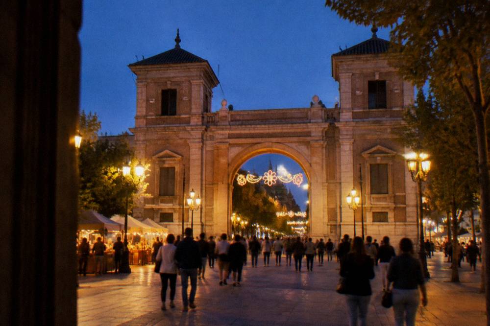 A city gate archway decorated for a festival with crowds walking beneath it in evening light