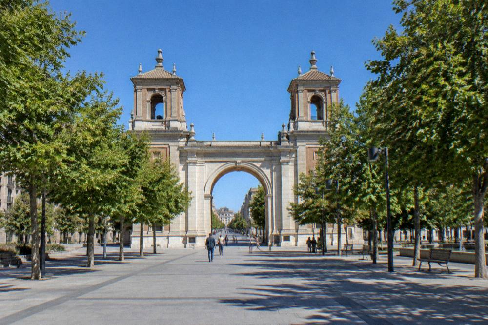 A stone archway gate seen from a distance down a straight city avenue with trees on both sides