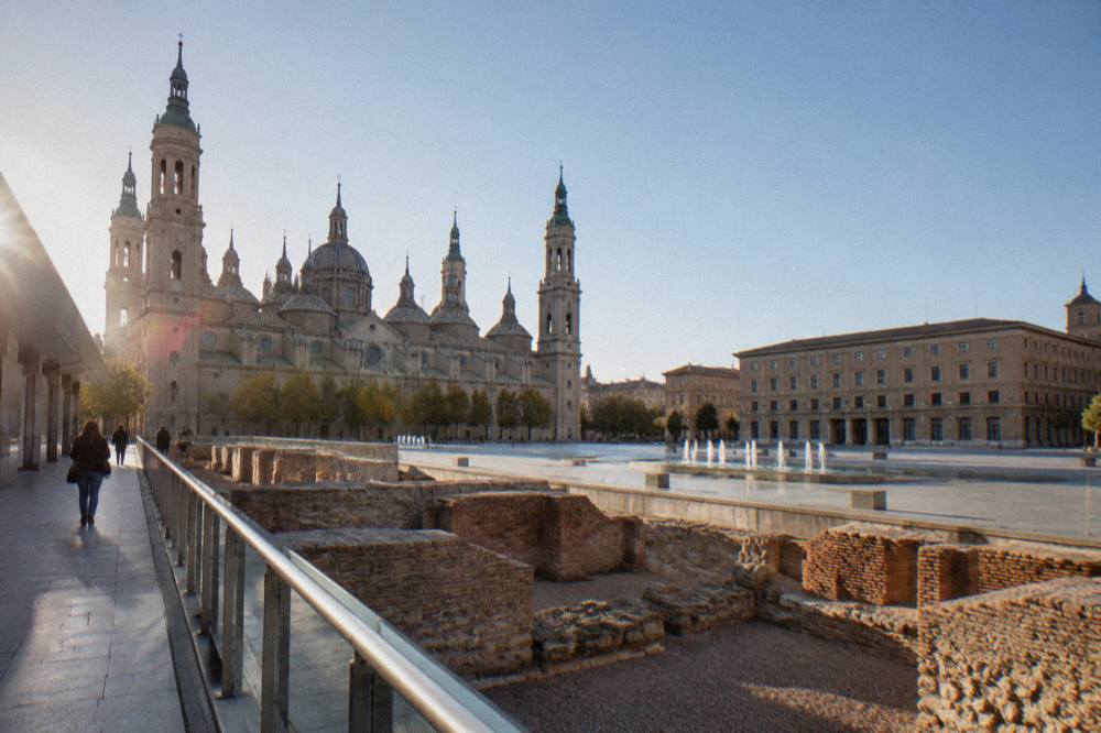 A museum walkway passing alongside exposed Roman brick and stone bath structures in Zaragoza