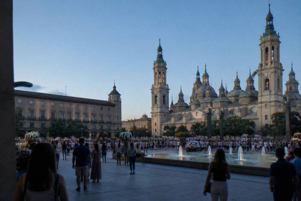 Crowds filling a central Zaragoza square during a festival with flowers and banners