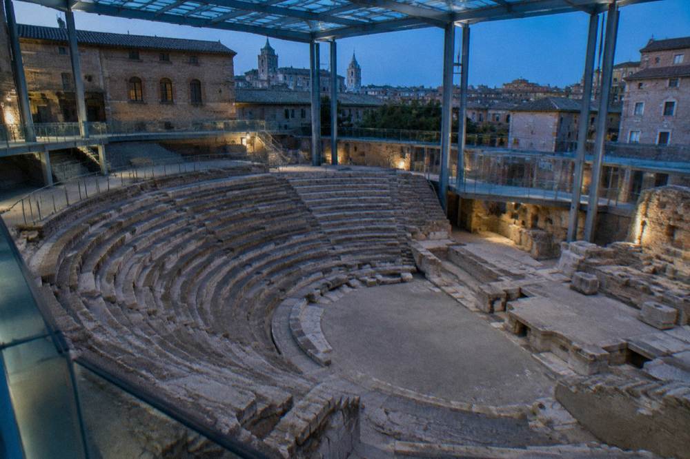 Curved stone tiers of an excavated Roman theatre seen from above inside a museum