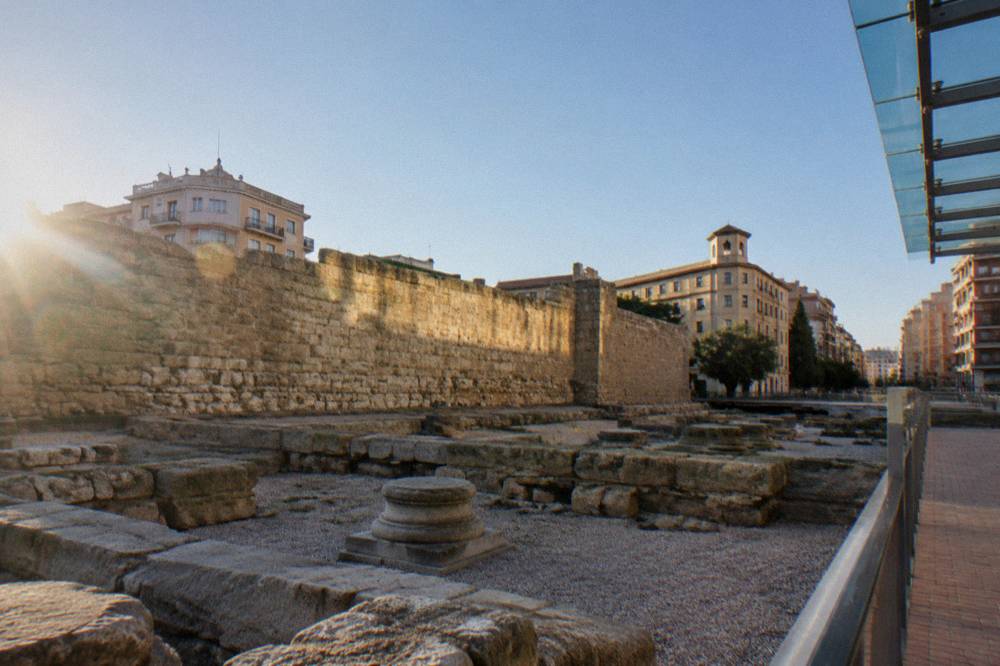 Sunlit stretch of ancient stone wall standing between modern city buildings