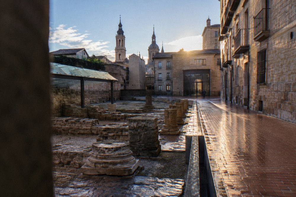 Narrow old-town street with stone buildings leading toward a museum entrance