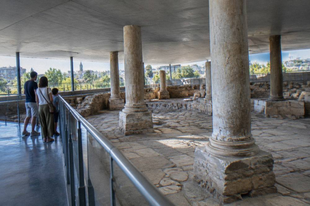 Family visitors looking at Roman stone remains behind a railing in Zaragoza