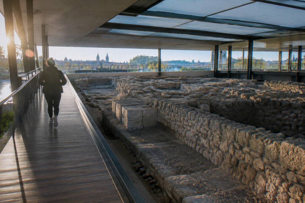 Visitor walking through a modern museum corridor above ancient stone foundations
